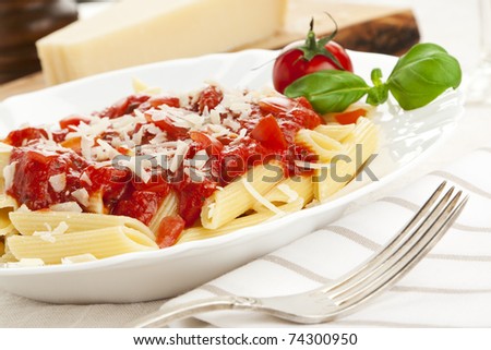 penne with tomato sauce and grated cheese, garnished with tomato and basil leaves, tilted view