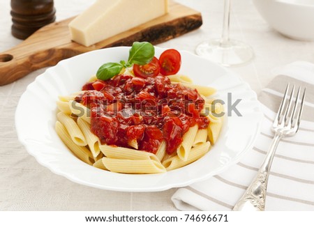 penne pasta with tomato sauce, garnished with basil, parmesan cheese and pepper mill in background