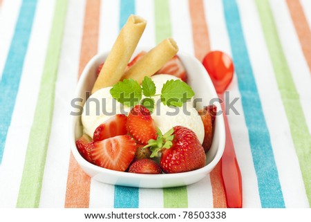 bowl with three scoops of vanilla ice cream with strawberries, waffles and red plastic spoon on striped table-cloth