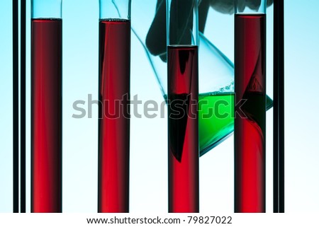 test tubes filled with red liquid, hand holding beaker with green liquid in background
