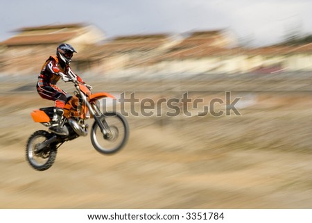 Motorcycle flying over a dirt ramp.  Frozen with a sense of motion.