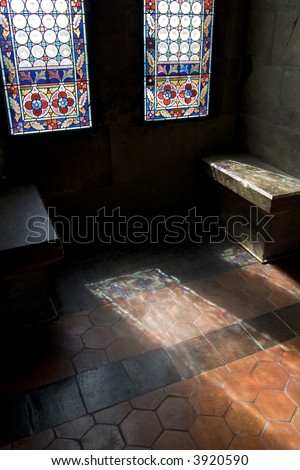 Light shines through a stained glass window onto a wooden floor in a medieval building.