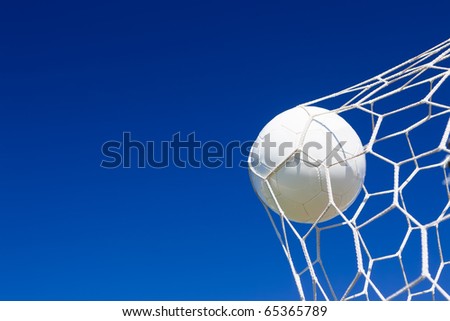 Close-up of a soccer ball (football) going into the back of the net with a blue sky background.