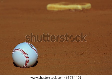 Close-up of a baseball on the infield dirt of a baseball diamond with a base in the background.
