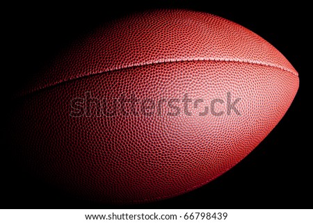 Close-up of an american football with dramatic side lighting on a black background.