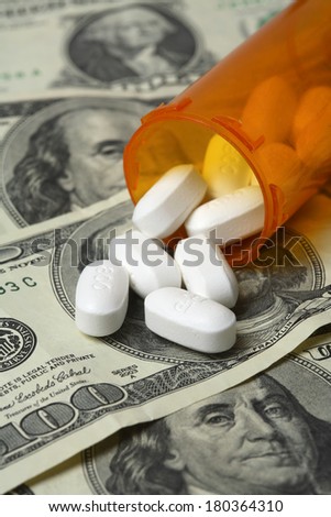 Bottle of pills spilling onto one hundred dollar bills