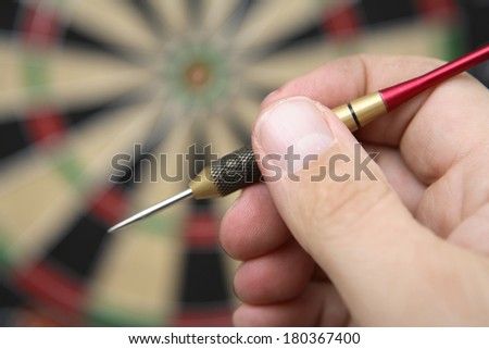 Hand holding dart next to darkboard