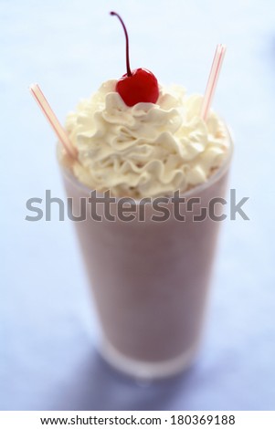 Strawberry milkshake beverage with cherry on top and two straws, on blue background