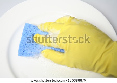 Hand in yellow latex glove cleaning white plate with blue sponge