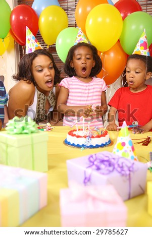 Young girl blowing out birthday candles with help from mother and brother