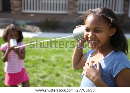 Two young girls playing telephone with cans and string