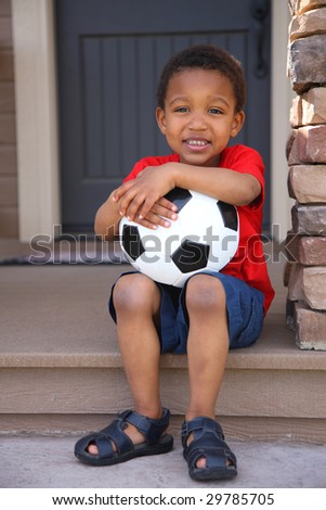 Young boy with soccer ball sitting on porch