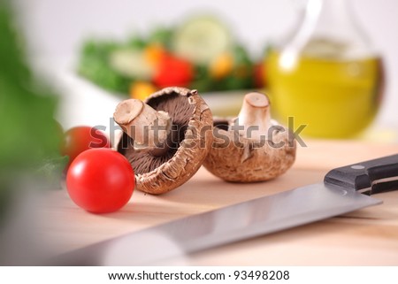 Mushrooms and cherry tomatoes on cutting board with salad and oil in background