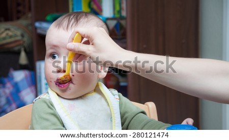 Mother feeding a funny looking baby with a spoon with blueberry jam