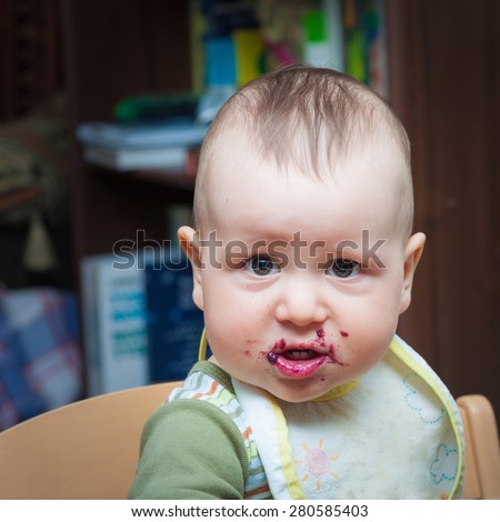 Adorable baby with bib and mouth stained with blueberry jam