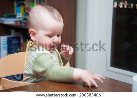 Cute baby with mouth stained with blueberry jam playing with the cap of the jar