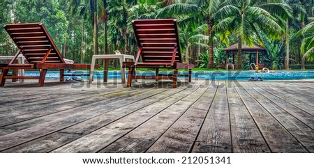 Wooden sunbath chair and side table in luxury swimming pool with hut and wooden pool deck in garden of resort