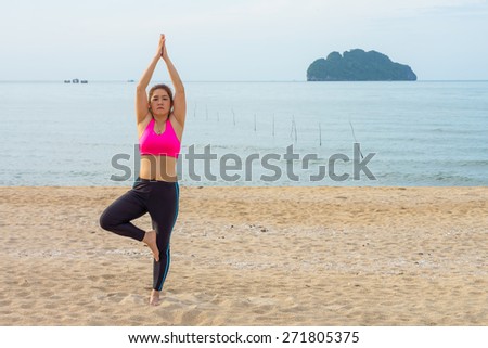 Thai woman poses a standing asana yoga or vriksasana or tree pose on the beach