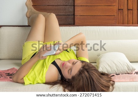 Charming asian woman is playing and chatting with her mobile phone on sofa in a room
