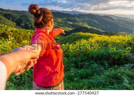 Red cloth woman leads her lover by the hand on mountain of Tithonia diversifolia field in the evening, Northern Thailand