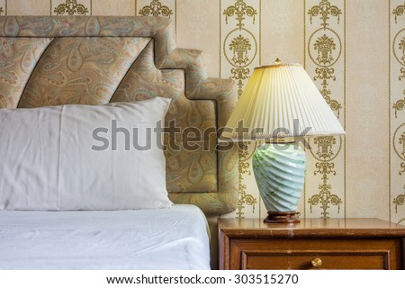 Vintage interior with jade stone desk lamp, bed, headboard, wooden nightstand and wallpaper in bedroom