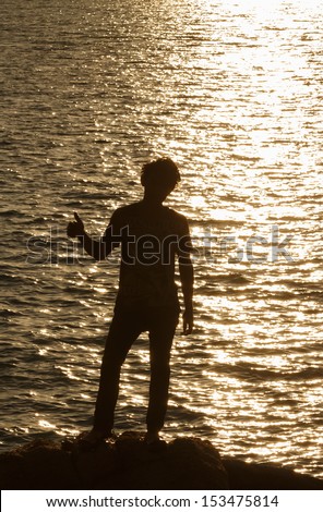 Man silhouette in victory action over sea sunset