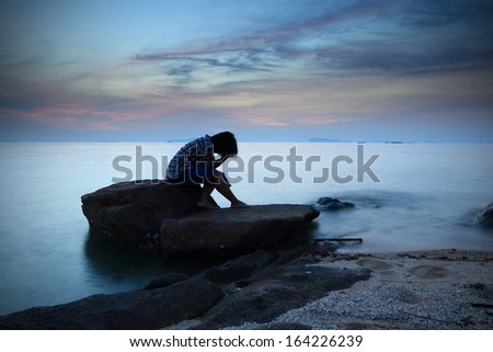 Woman  sitting and contemplating alon on the rock by the beach