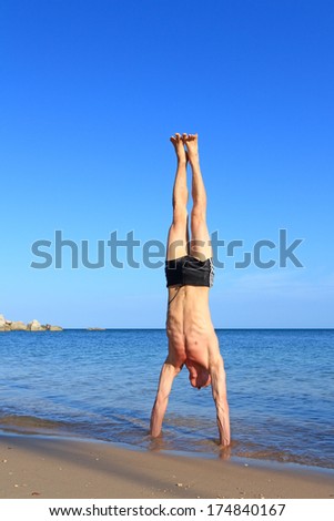 Man doing yoga Handstand pose by the beach at morning sunlight