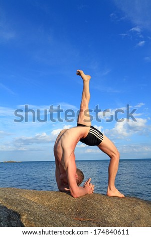 Man doing yoga Wheel pose by the beach at morning sunlight