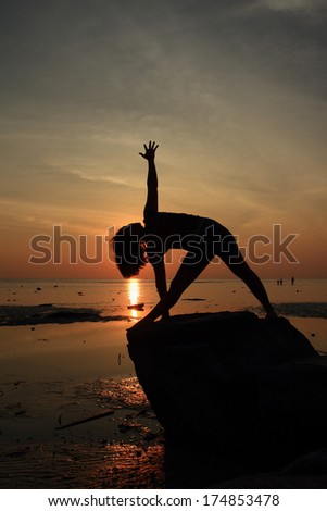 Silhouette yoga girl by the beach at sunrise doing Triangle Pose