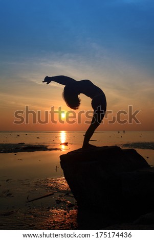 Silhouette yoga girl doing Wheel pose on rock by  beach sunset