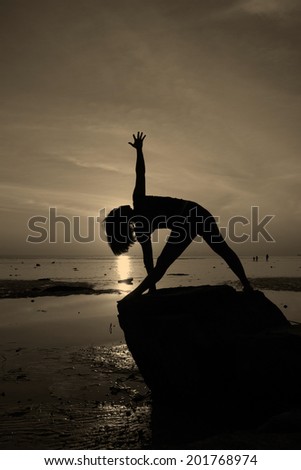 Silhouette vintage  yoga girl by the beach at sunrise Triangle  pose on rock