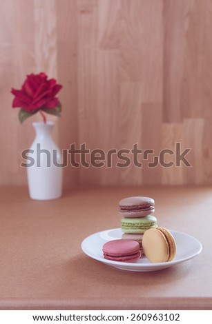 French sweet delicacy macaroons and red rose on grunge wood table