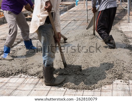 Construction workers spreading freshly poured concrete mix for house building