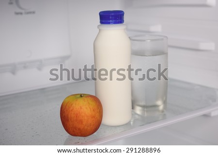 Milk bottles,glass of water and apple in refrigerator