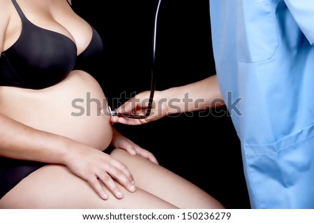A beautiful young pregnant woman is being examined by her doctor. Isolated on black background.