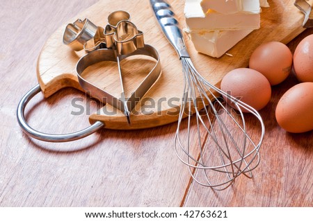 Baking ingredients with eggbeater and cake tin on a wooden kitchen-board