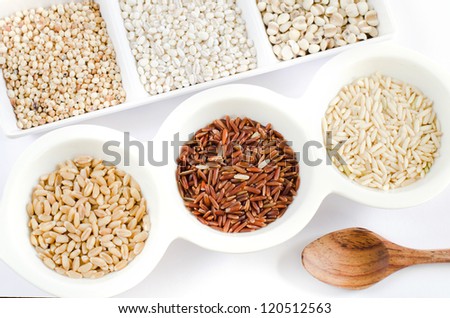 top views of grain and wooden spoon ,  rice , red rice , wheat,  job\'s tears , barley and millet grains on white bowl