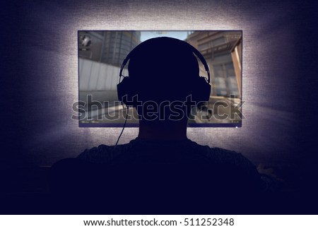 Gamer in headphones sits in front of a blank monitor in dark room