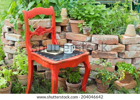 red chair in a garden with herbs, cup and books/chair/garden