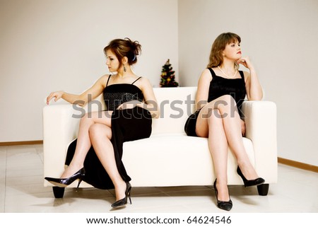 two beautiful woman sitting on the different sides on sofa