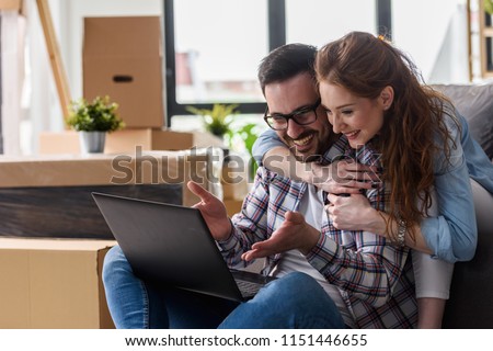 Young couple moving in new home. Sitting and relaxing after unpacking. Searching home decorating ideas on laptop
