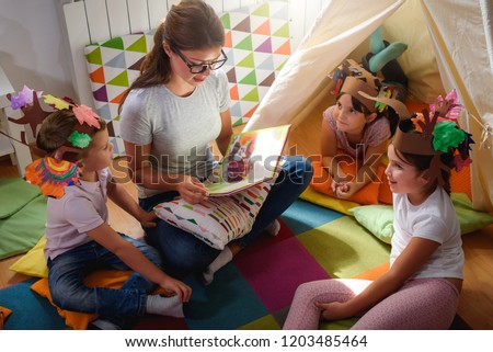 Preschool teacher reading a story to children at kindergarten. Mother reading to the children.