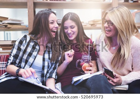 Three young female college students with books looking tablet and laughing
