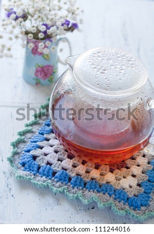 Crochet pothodler with a teapot with flowers in the distance