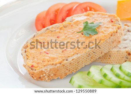 Close Up Image of Two Sesame Bread Slices with Hummus Spread, Tomato, Cucumber and Cheese on a White Plate
