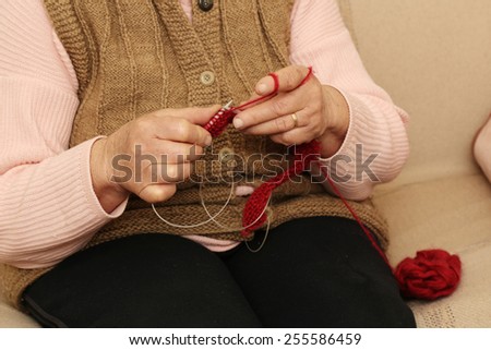 Hands knitting close-up Elderly woman knitting with red wool.