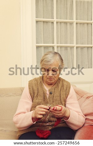 Elderly woman knitting with red wool, Portrait of grandmother knitting with red wool and sitting on the couch