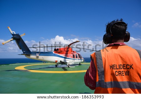 Shut down helicopter with helipad crew on jack up oil rig with blue sky