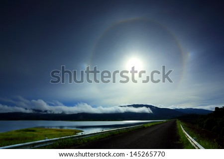 Amazing sun halo above rural road with lake and mountains